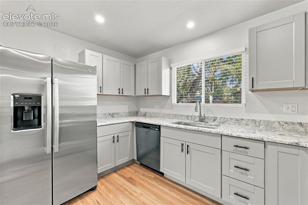 Image 10 of 49: Kitchen featuring light wood-finish flooring, light gray cabinetry with bla