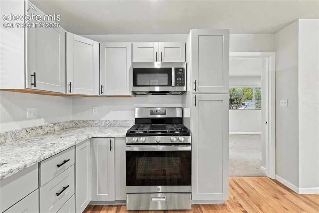 Image 11 of 49: Modern kitchen featuring light gray shaker cabinetry, stainless steel appli