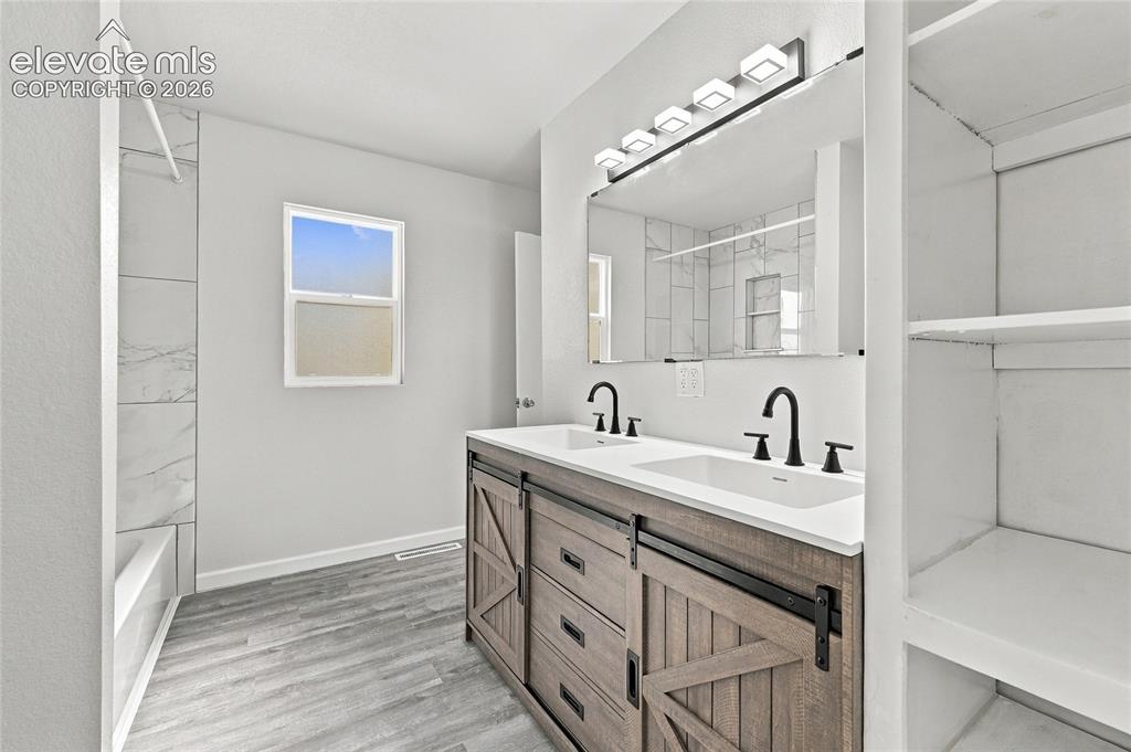 Image 24 of 49: Dual vanity with integrated sinks, wood-finish cabinetry, black fixtures, a