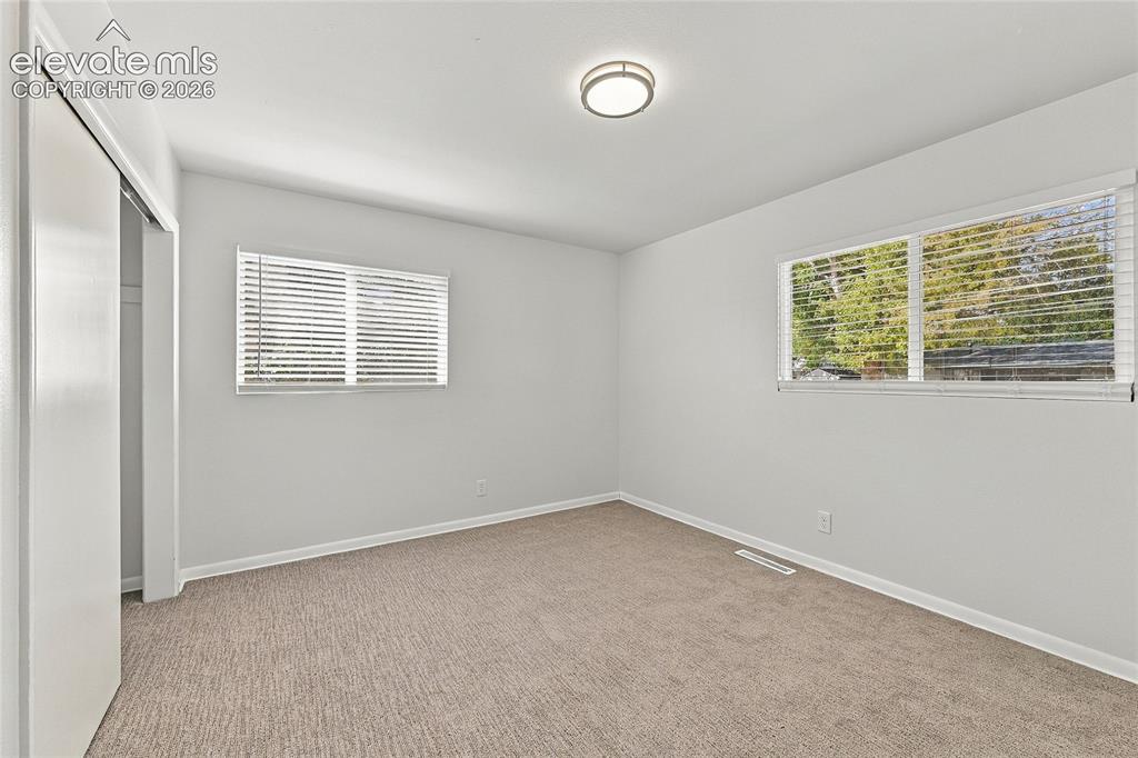 Image 25 of 49: Light-colored carpeting, two windows with horizontal blinds, and a flush-mo