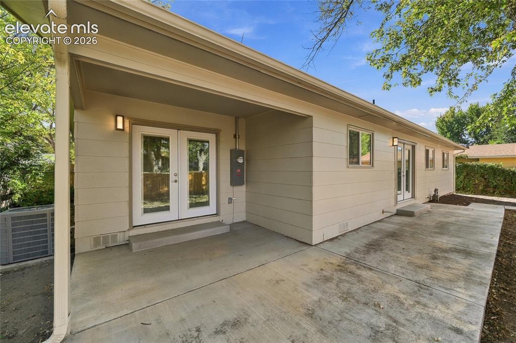 Image 30 of 49: Expansive concrete patio with covered area, double glass-paneled doors, and