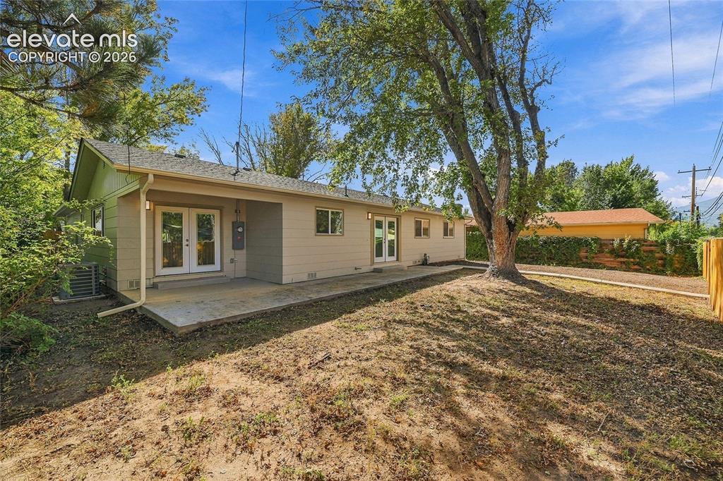 Image 34 of 49: Rear exterior featuring a large tree, concrete patio, and a light-colored f