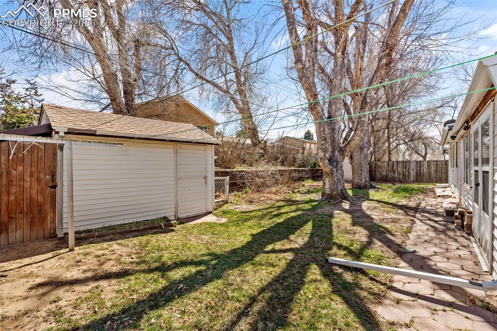 Image 16 of 18: Fenced backyard with an outbuilding and a patio