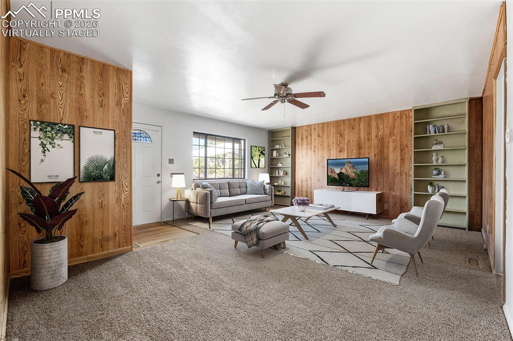 Image 3 of 18: Living area featuring built in shelves, wood walls, light colored carpet, a
