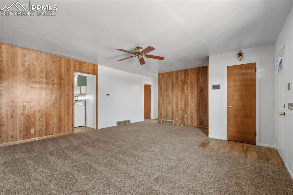 Image 4 of 18: Unfurnished living room with wood walls, light carpet, and ceiling fan