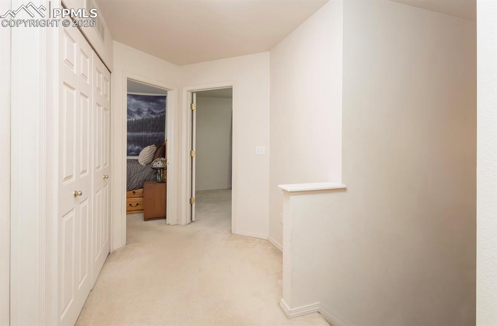 Image 25 of 35: Carpeted hallway featuring white walls, bifold closet doors with brass-tone