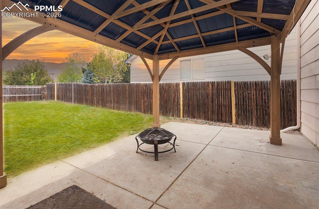 Image 34 of 35: Covered patio with a corrugated metal roof, wood-frame gazebo, concrete pat