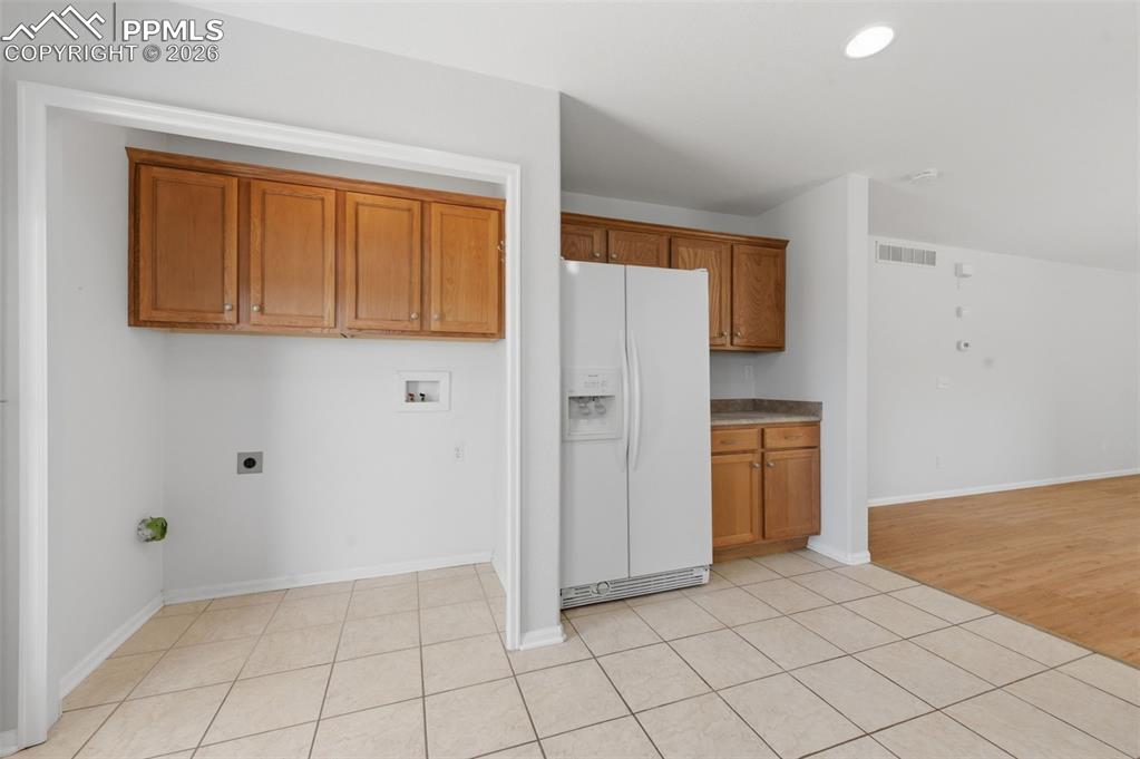 Image 16 of 34: Utility area with neutral tile flooring, overhead cabinetry, and appliance 
