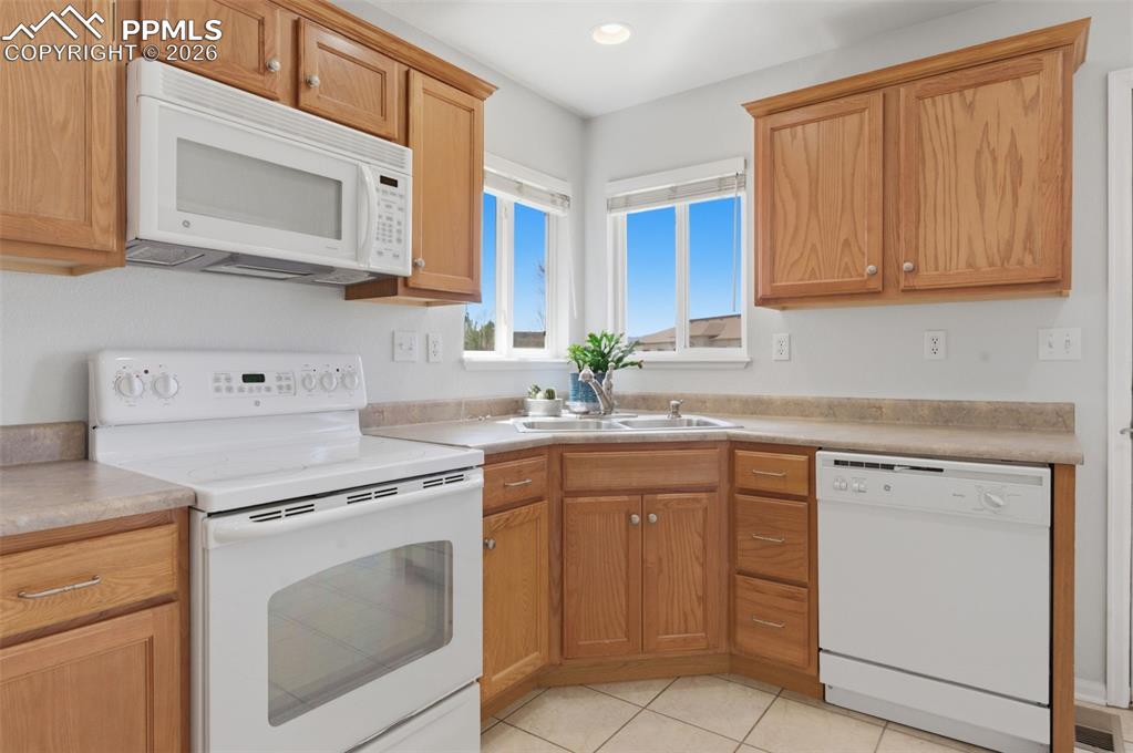 Image 17 of 34: Kitchen featuring wood cabinetry, white appliances, and a corner sink posit