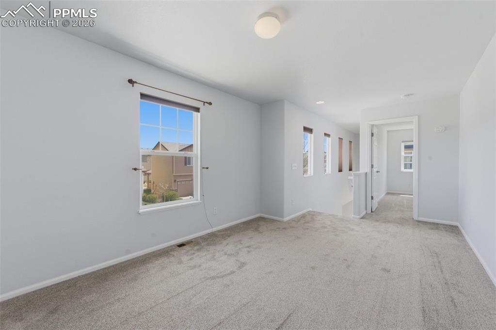 Image 21 of 34: Spacious carpeted room featuring a large window with a dark curtain rod, li