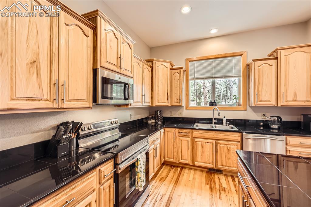 Image 10 of 50: Kitchen featuring light brown cabinetry, a sink, appliances with stainless 