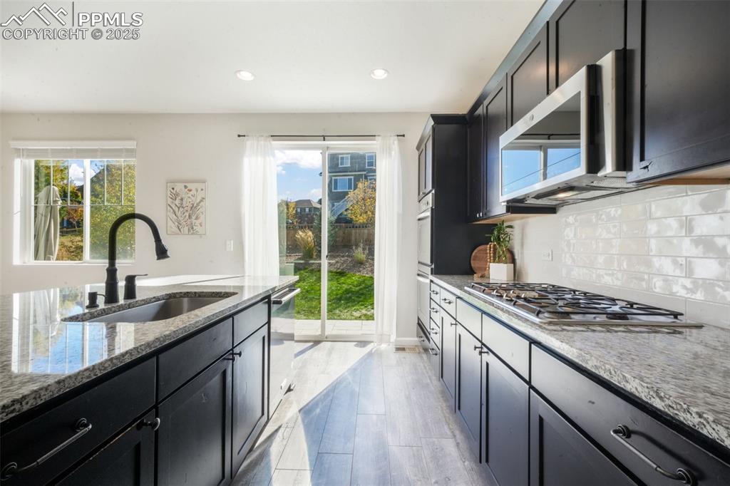 Image 17 of 50: Kitchen featuring dark cabinets, light stone counters, tasteful backsplash,