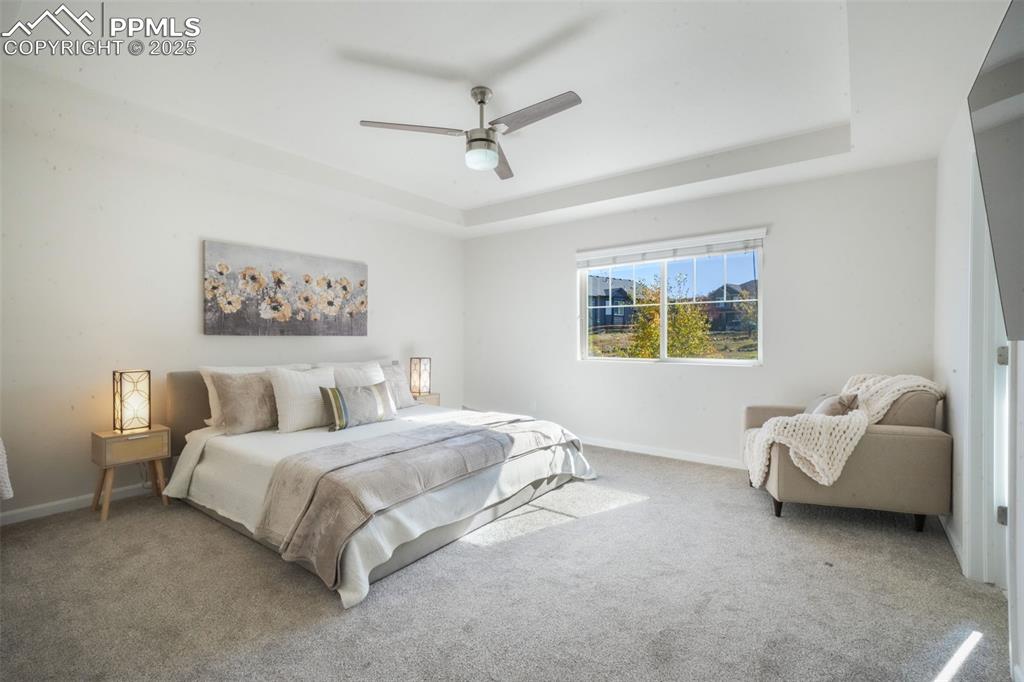 Image 24 of 50: Carpeted bedroom featuring a tray ceiling and ceiling fan