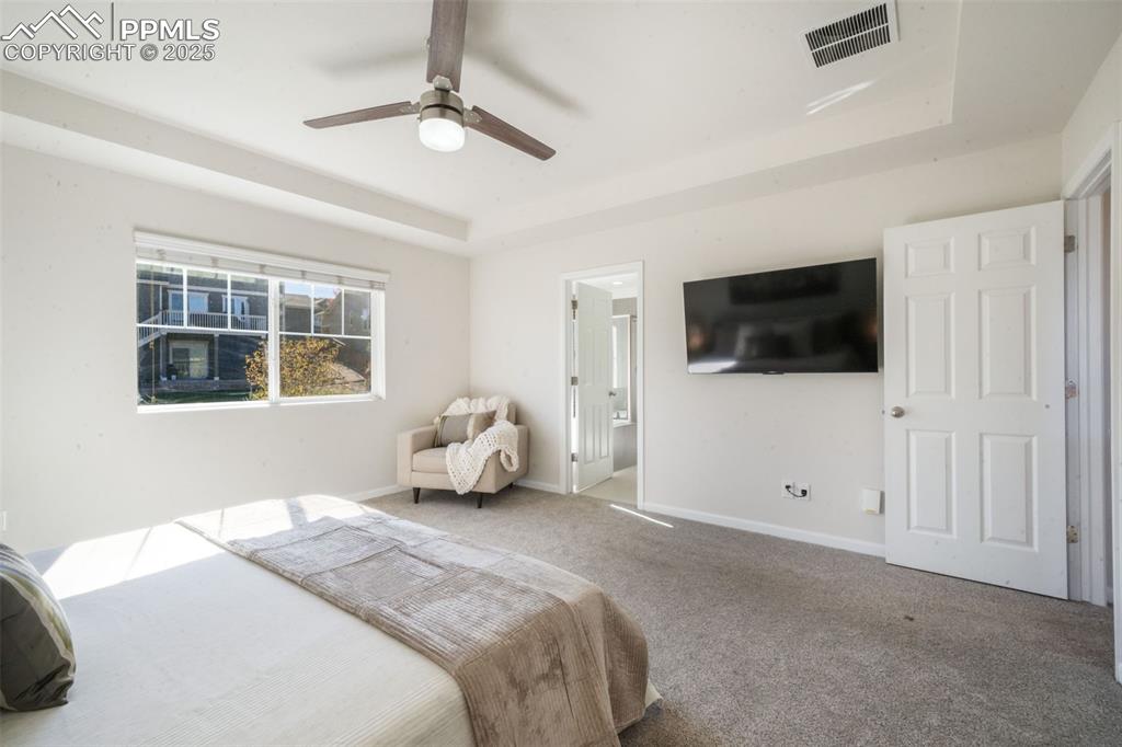 Image 25 of 50: Carpeted bedroom featuring a tray ceiling, ensuite bath, and a ceiling fan