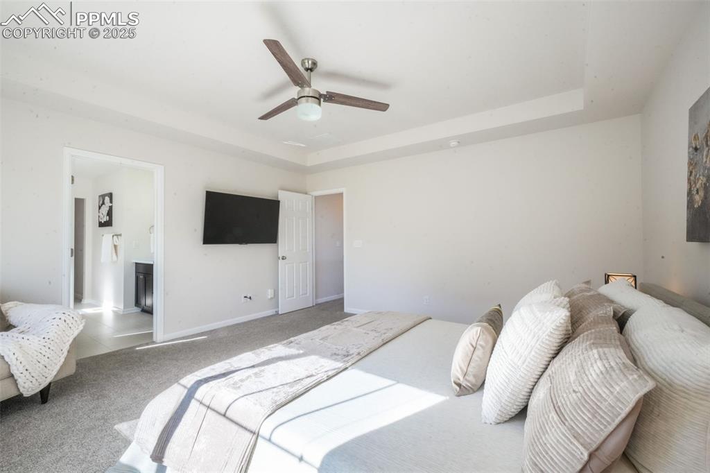 Image 26 of 50: Bedroom with a raised ceiling, carpet floors, ceiling fan, and ensuite bath
