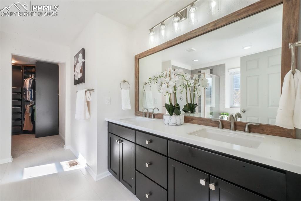 Image 27 of 50: Bathroom featuring double vanity, a walk in closet, a shower stall, and lig
