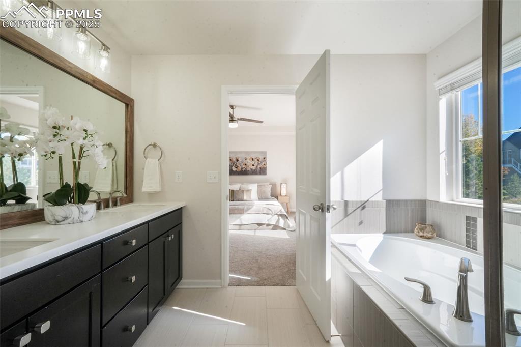 Image 28 of 50: Ensuite bathroom featuring a garden tub, double vanity, a ceiling fan, and