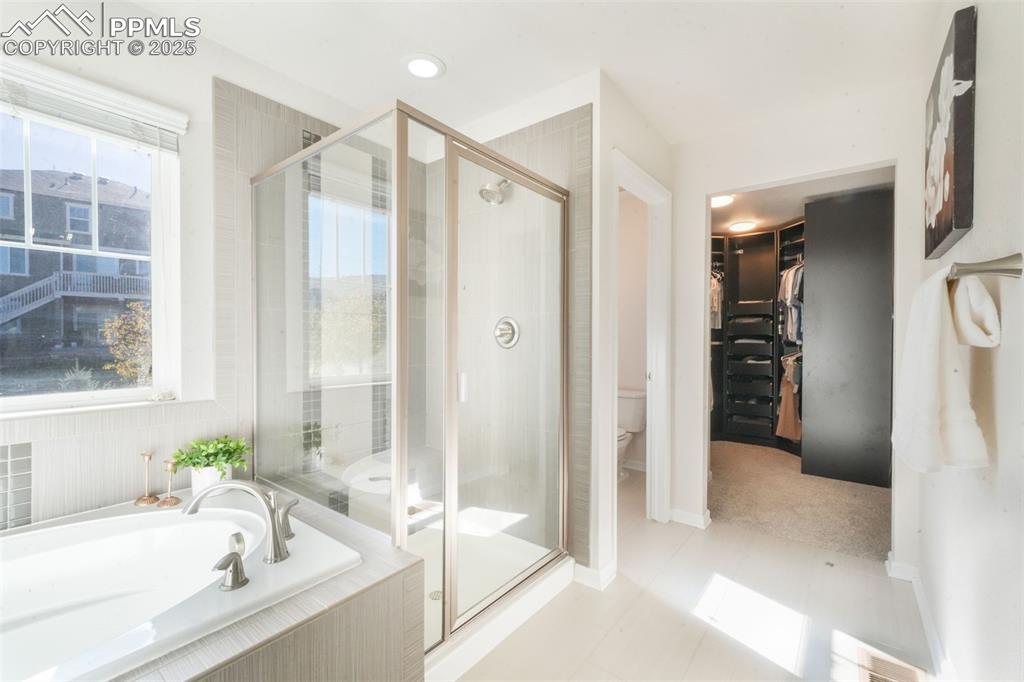 Image 29 of 50: Bathroom featuring a spacious closet, a bath, a stall shower, light tile pa