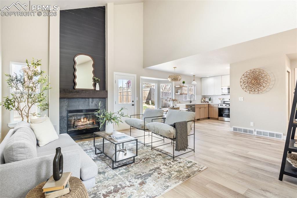 Image 6 of 26: Living area with light wood-type flooring, a fireplace, and vaulted ceiling
