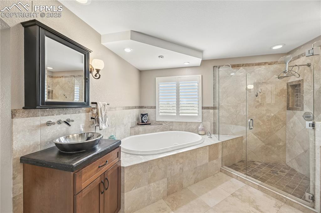 Image 27 of 40: Full bath featuring vanity, a shower stall, a bath, tile walls, and tile pa