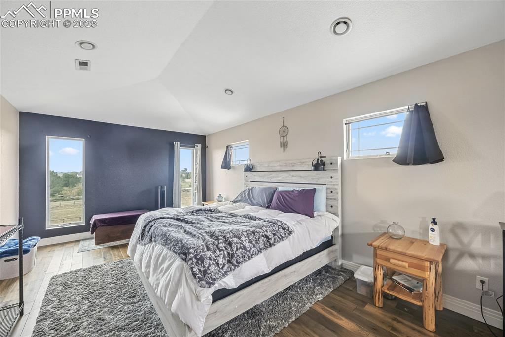 Image 30 of 40: Bedroom with wood finished floors, multiple windows, and vaulted ceiling