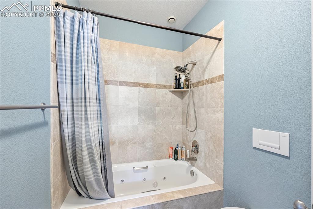 Image 34 of 40: Bathroom featuring a textured wall, a combined bath / shower with jetted tu