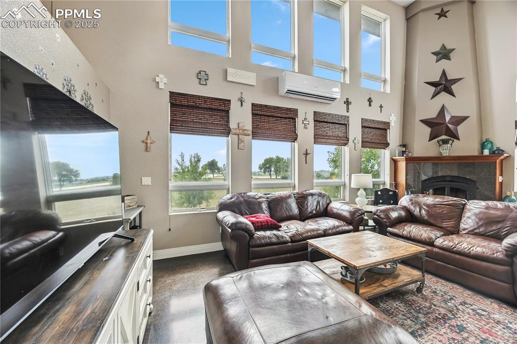 Image 5 of 40: Living area with a tile fireplace, a high ceiling, and an AC wall unit
