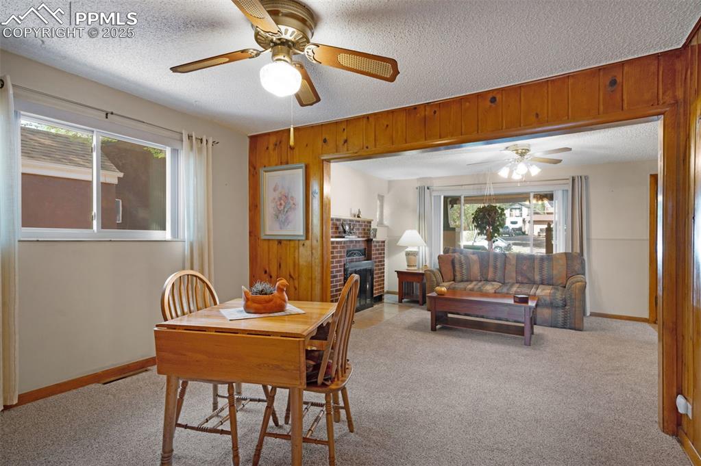 Image 10 of 27: Dining space with light colored carpet, wood walls, a fireplace, and a text