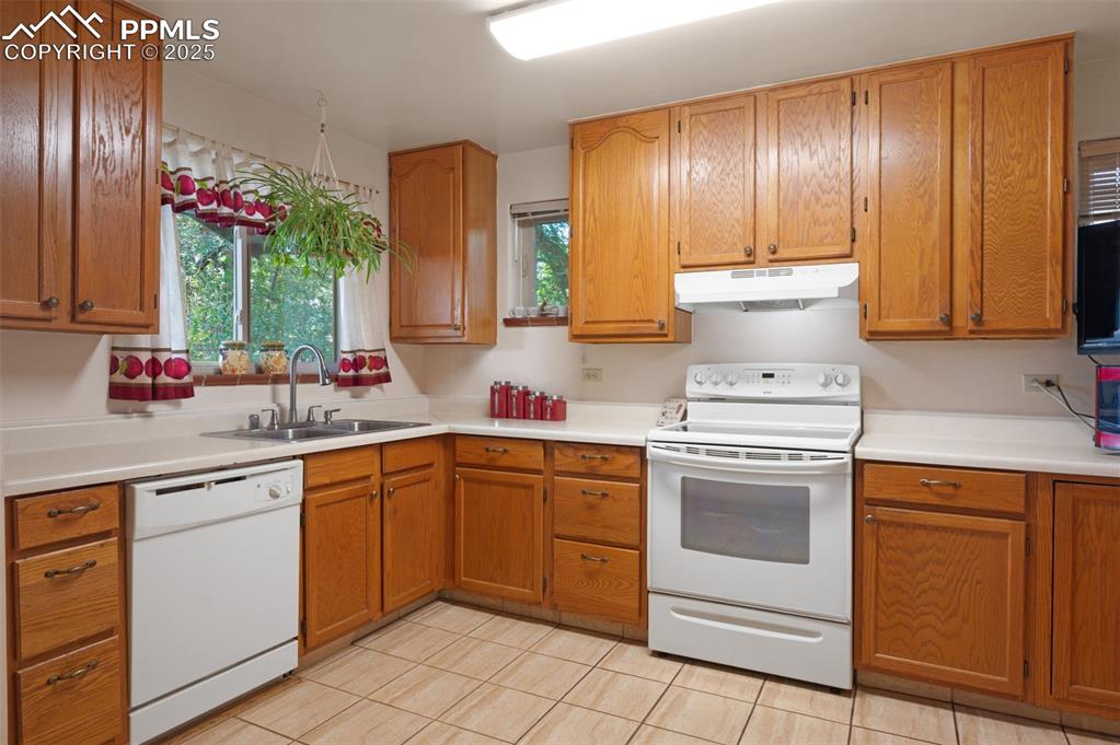 Image 11 of 27: Kitchen featuring white appliances, brown cabinets, light countertops, unde