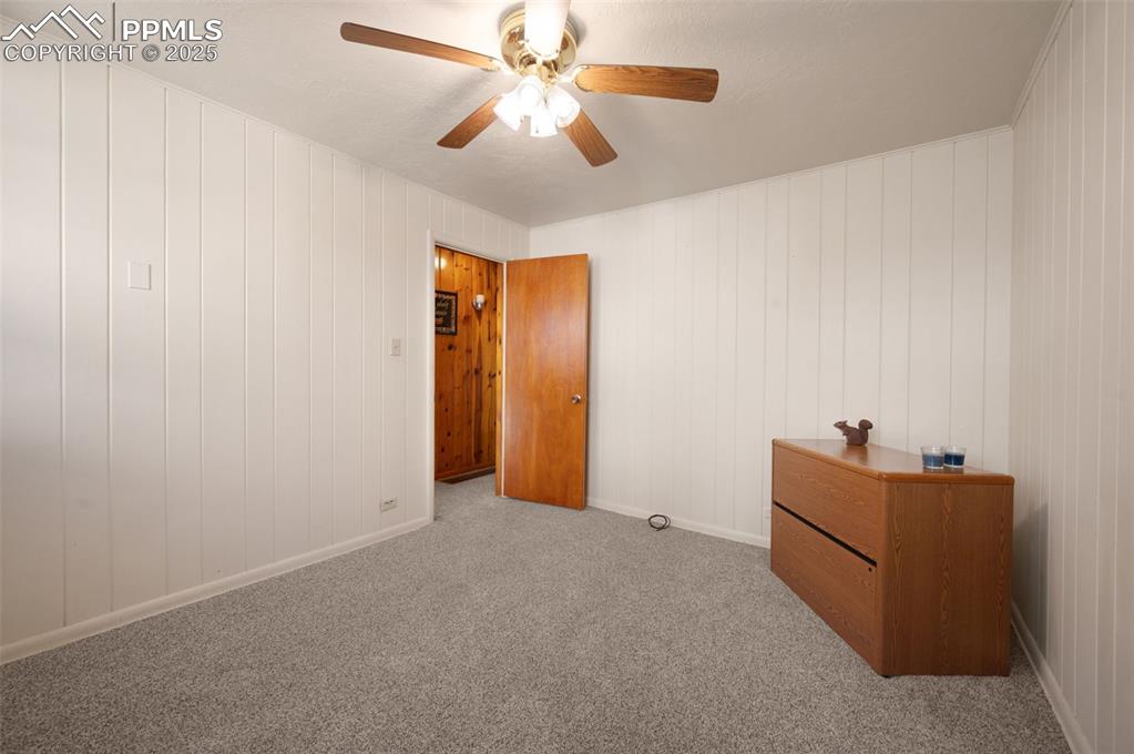 Image 20 of 27: Unfurnished bedroom featuring carpet flooring, ceiling fan, and wood walls