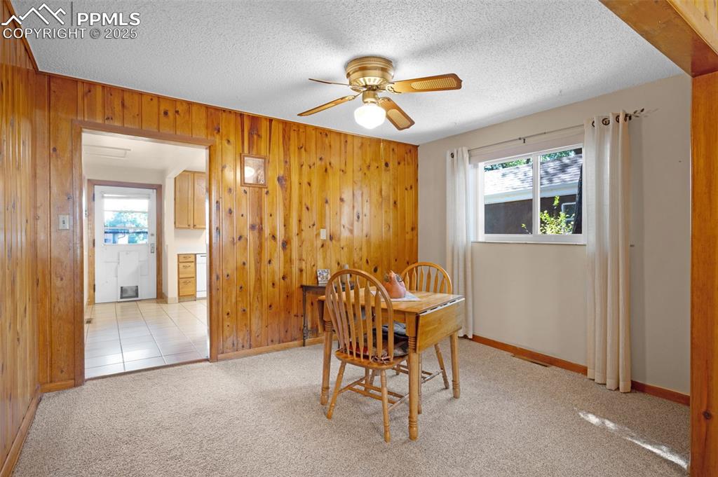Image 9 of 27: Carpeted dining area with wood walls, a ceiling fan, and a textured ceiling