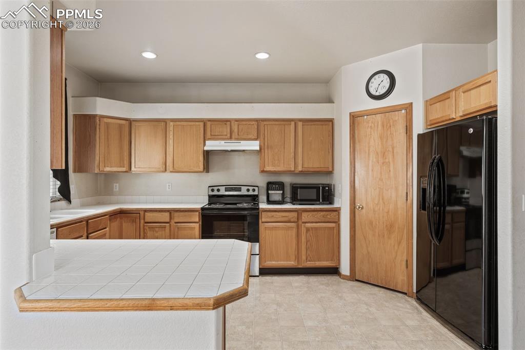 Image 10 of 40: Kitchen featuring wood cabinetry, white tile countertops, recessed lighting