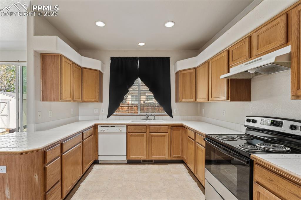 Image 11 of 40: U-shaped kitchen featuring wood-finish cabinetry, white countertops, recess