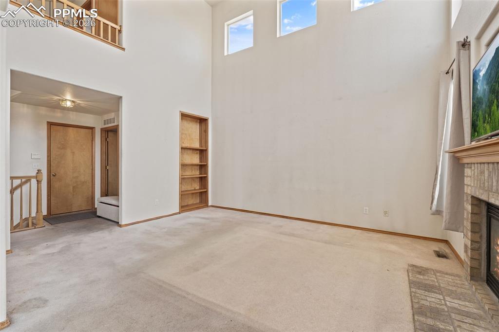 Image 18 of 40: Two-story living area featuring a brick fireplace, built-in shelving, high 