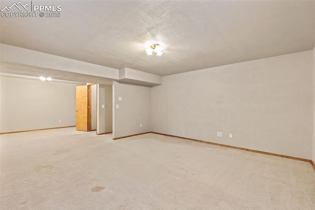 Image 32 of 40: Expansive carpeted room featuring light neutral wall paint, wood trim, and 