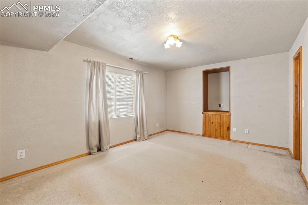 Image 34 of 40: Carpeted room with a ceiling-mounted light fixture, a window with horizonta
