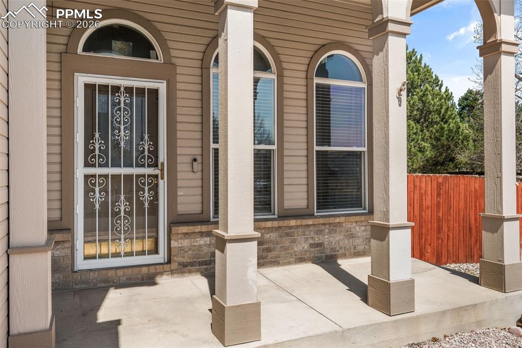 Image 4 of 40: Covered concrete porch with decorative columns, featuring a white security 