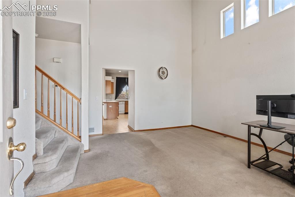 Image 5 of 40: Entryway featuring a carpeted staircase with wood banister and an open livi