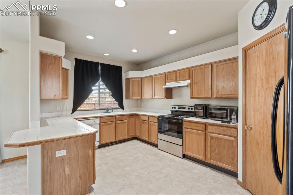 Image 9 of 40: Kitchen featuring light wood cabinetry, white tile countertops, recessed li