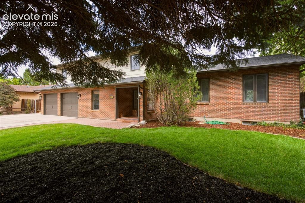 Image 1 of 32: Brick exterior with a three-car garage, paved driveway, and mature landscap
