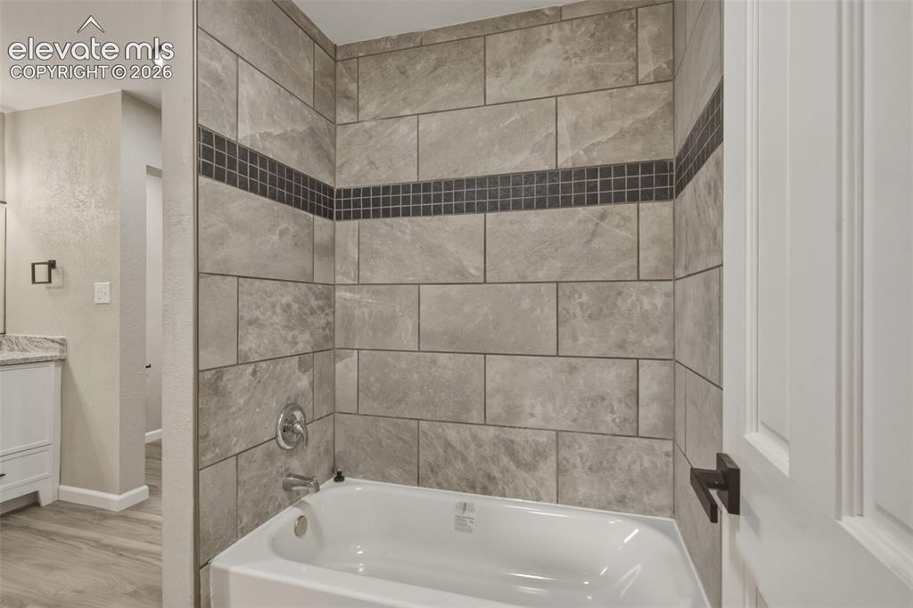 Image 10 of 32: Bathtub with integrated shower, gray large-format tile surround, mosaic acc