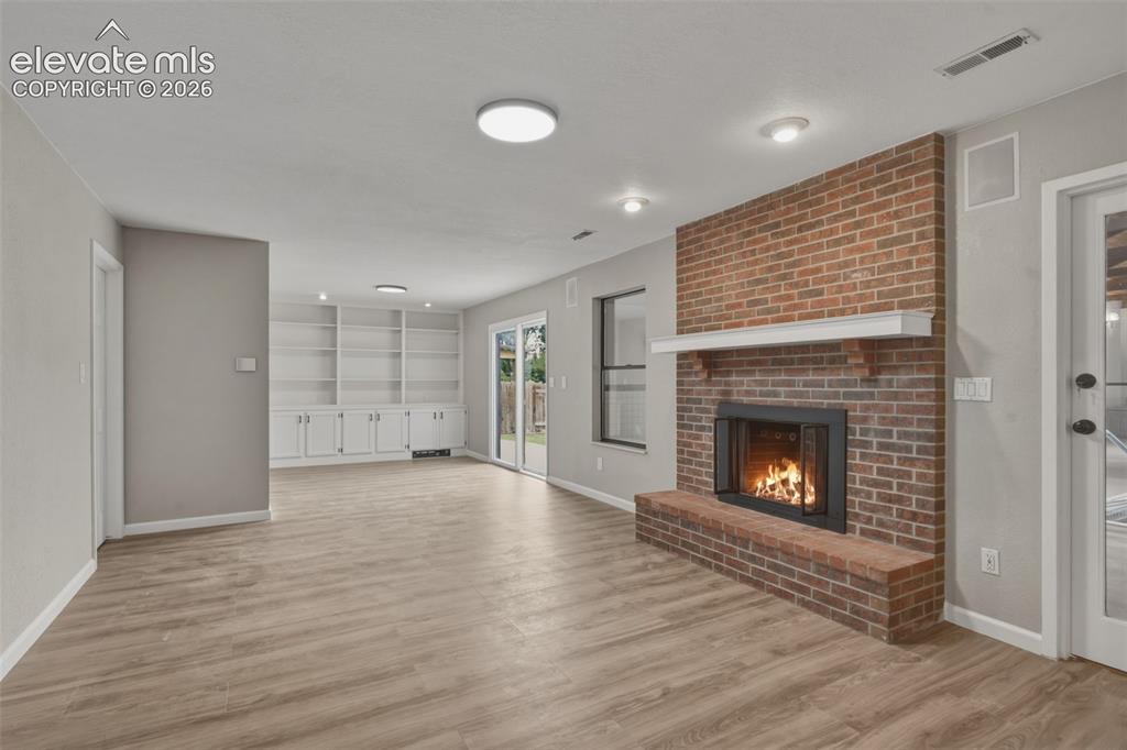 Image 19 of 32: Brick-clad fireplace with a hearth, built-in shelving, wood-finish flooring
