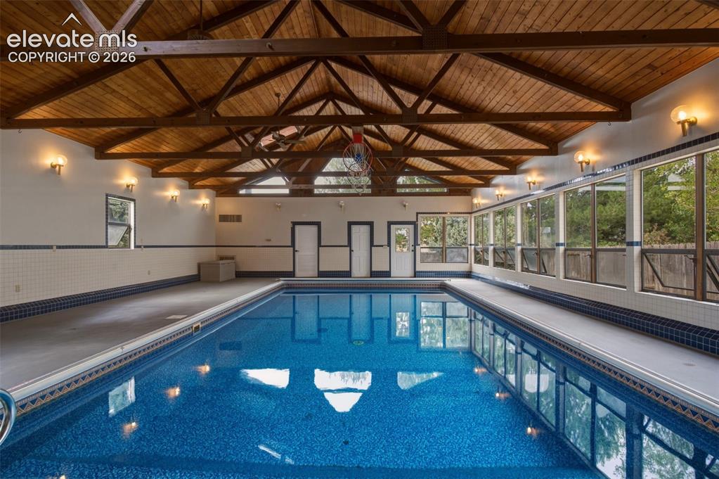 Image 2 of 32: Indoor swimming pool with exposed wood beam ceiling, expansive windows, blu
