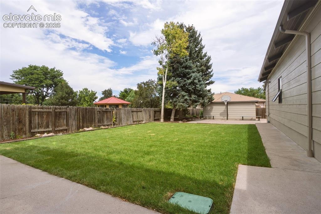 Image 25 of 32: Expansive green lawn, mature trees, wood privacy fencing, and concrete path