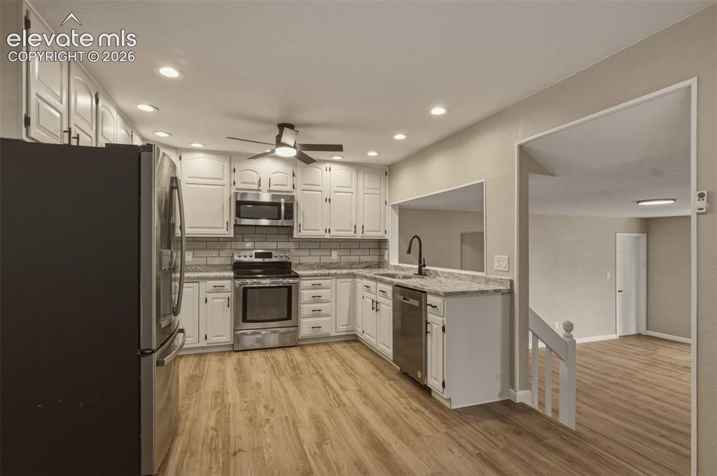 Image 6 of 32: Contemporary kitchen featuring wood-finish flooring, white cabinetry, integ