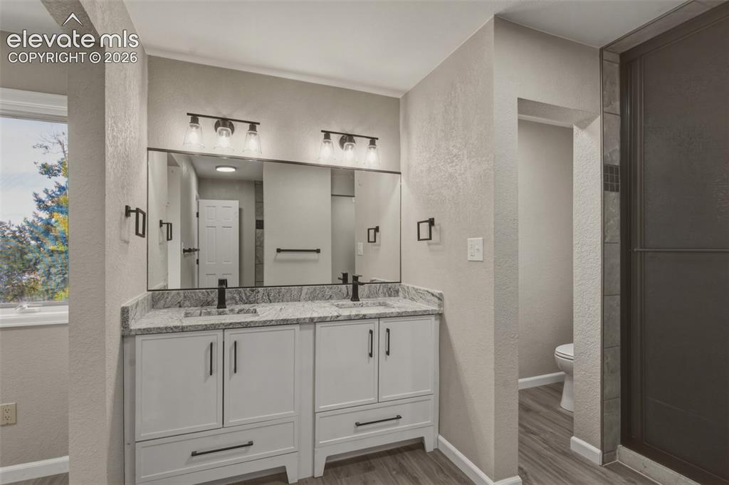 Image 8 of 32: Dual vanity with stone-finish countertop, wood-finish flooring, framed mirr