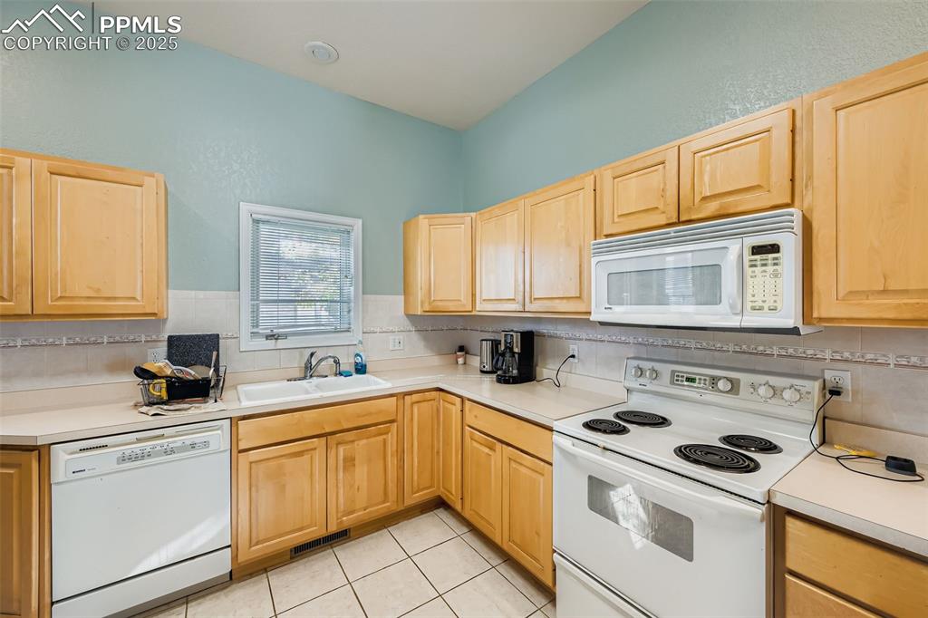 Image 5 of 11: Kitchen with white appliances, light brown cabinetry, and light countertops