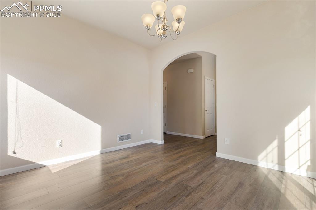 Image 15 of 42: Spare room featuring a chandelier, arched walkways, and wood finished floor