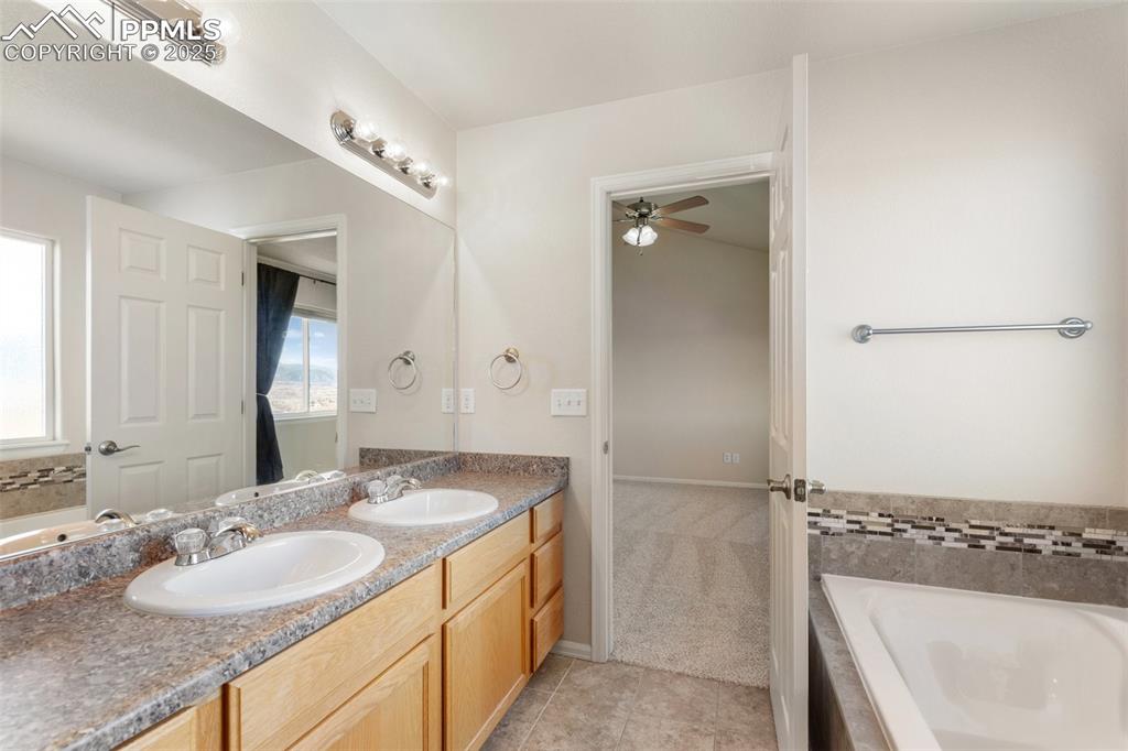 Image 24 of 42: Bathroom with double vanity, a relaxing tiled tub, light tile patterned flo