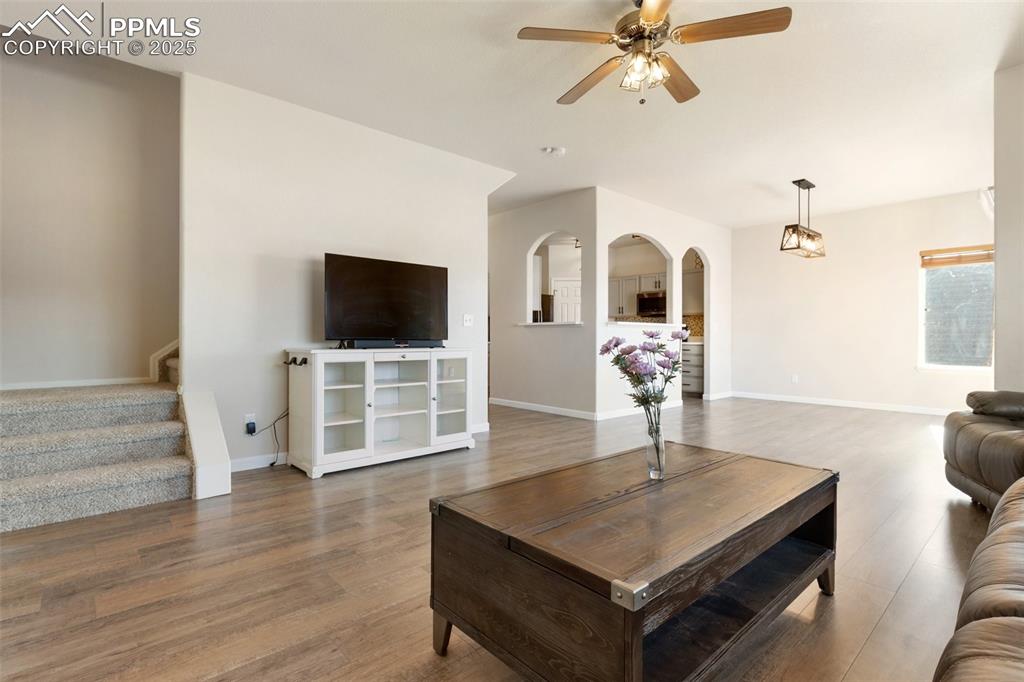 Image 5 of 42: Living room with stairs, wood finished floors, ceiling fan, and arched walk